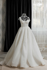 Fototapeta premium A white dress with a lot of sparkles on it is hanging on a mannequin. The dress is long and flowing, giving off a sense of elegance and sophistication. The mannequin is positioned in front of a window