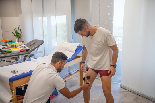 Osteopath practising physiotherapy on a man's leg with the help of electrodes