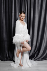 A woman in a white gown with a feathery sleeve is posing for a photo. Concept of elegance and sophistication, as the woman is dressed in a beautiful wedding gown