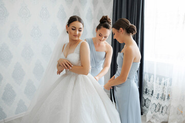 A bride is getting ready for her wedding with her bridesmaids. The bride is wearing a white dress...