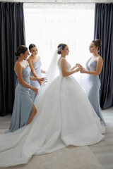 A bride is getting ready for her wedding with her bridesmaids. The bride is wearing a white dress...