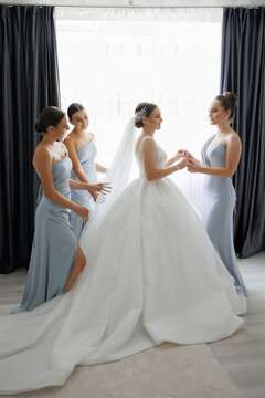 A bride is getting ready for her wedding with her bridesmaids. The bride is wearing a white dress and the bridesmaids are wearing blue dresses