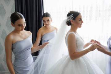A bride is getting ready for her wedding with her bridesmaids. The bride is wearing a white dress and a veil