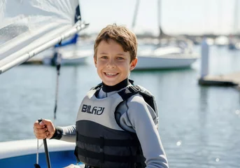 Fotobehang Portrait of smiling young caucasian boy wearing life jacket sailing dinghy on sunny day © Running opossum