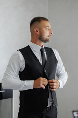 A man in a black vest and white shirt is adjusting his tie. Concept of formality and professionalism, as the man is dressed in a suit and tie