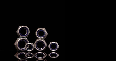Steel nuts of different sizes on black background with reflecting dark surface. Close up macro shot with copy space