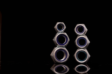 Steel nuts of different sizes on black background with reflecting dark surface. Close up macro shot with copy space