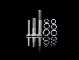 Steel nuts and bolts of different sizes on black background with reflecting dark surface. Black and white.
