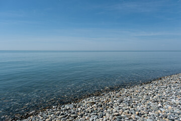 Calm shoreline with pebbles and a clear blue sky during a sunny day at the beach
