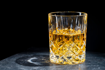 Crystal glass of whiskey with ice cubes on black background, closeup, copy space