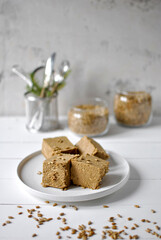 Pieces of halva made from sunflower seeds on a white plate. Glass jars with seeds in the background. Vertical location.