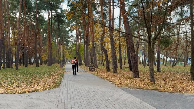 Municipal worker in uniform using leaf blower to clear fallen leaves in autumn park