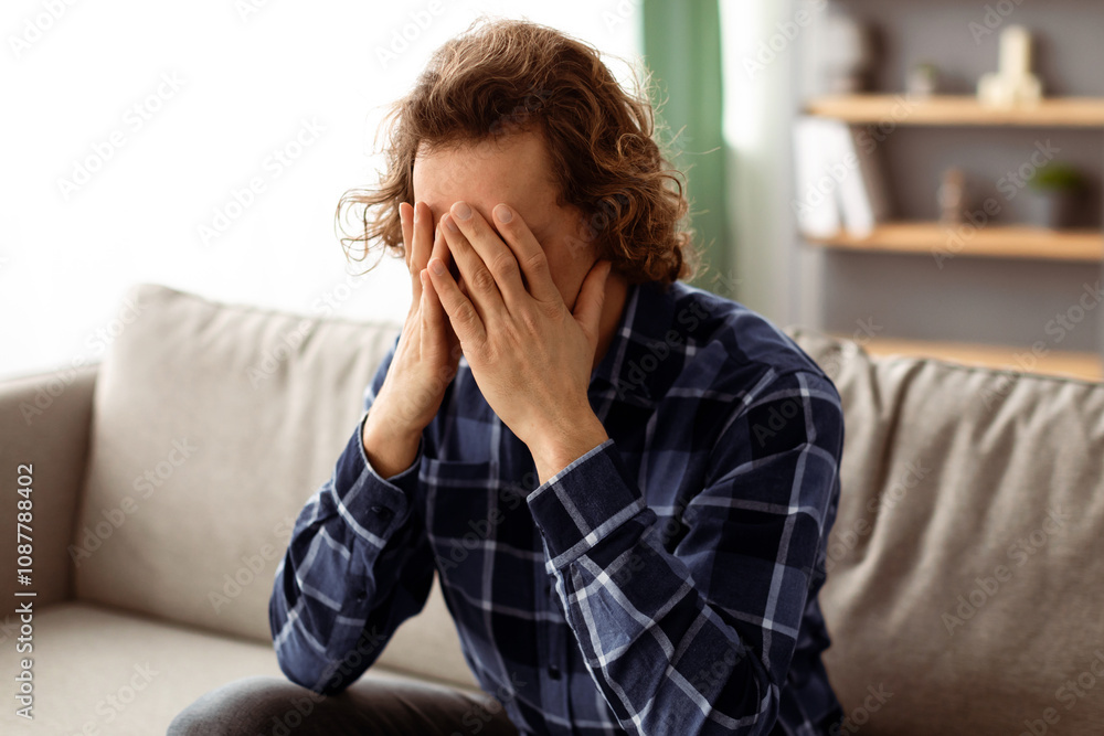 Aufkleber depression. unhappy guy covering face being tired of unsolved problems sitting on couch at home. unr