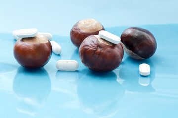 Treatment of autumn depression concept. White tablets positioned on and beneath chestnuts reflected on light blue background