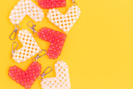Handcraft keychains in a heart shape made from acrylic beads scattered on a yellow background. Concept with place for text.