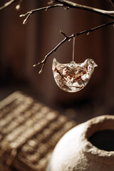 A handmade vase holds a graceful branch decorated with elegant glass ornaments. Sunlight streams through, casting warm, golden tones, highlighting the delicate textures. The New year is coming soon.