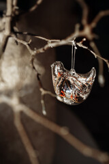 A handmade vase holds a graceful branch decorated with elegant glass ornaments. Sunlight streams through, casting warm, golden tones, highlighting the delicate textures. The New year is coming soon.