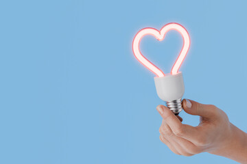 Hand holding a heart shaped light bulb on blue background