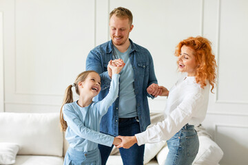 Fototapeta premium Family of three having fun, laughing and enjoying time at home, dancing together and holding hands, living room interior, free space