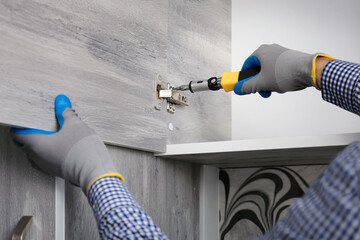 Close-up a hands man screws in kitchen shelf holders. Assembling furniture for home kitchen.