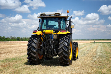 Rear view of a tractor yellow color standing in a field. A farmer checks the quality of the soil of an agricultural field.