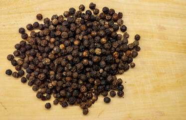 Black peppercorns piled on wooden cutting board.