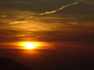 Colorful sky with yellow and orange colors, sunlight over dark misty horizon of mountain during sunset. Topics: tourism, weather, meteorology, sun energy, season, beauty of nature, air space, dusk