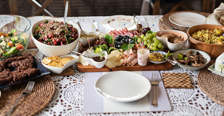 Breakfast on the table with napkin. Various of food prepared at home. Cold plate of salad, ham, cheese, olives and fruit. Fresh meal on board. Panoramic.