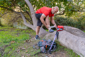 A hiker with his foot resting on a log, bandaging his ankle, concept of a first aid kit in the...