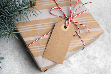 Christmas gift box with blank craft tag and fir tree on grey background, gift tag with copy space