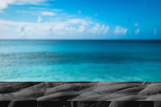 Empty black marble table with blur blue sky and sea bokeh background with green leaf foreground,Mock up template for display or montage of product or content use as banner in social media ads