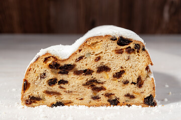 Cut in half stollen loaf on a table. Close-up of traditional German Christmas bread of dried fruits, nuts and spices coated with powdered sugar. Concept of sweet Cristmass breakfact.