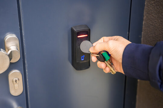 Close up view of person using a electric lock key fob to access a building via a reader of entry system mounted on a house wall