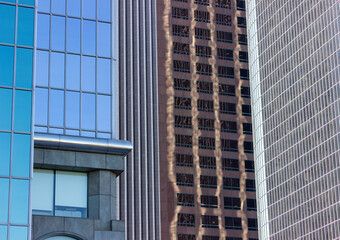 A close-up view of modern office buildings in downtown Los Angeles. The buildings feature sleek glass facades that reflect the surrounding structures, creating an intricate pattern of reflections.