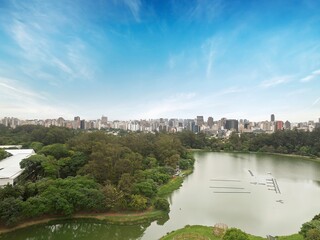 Obraz premium Vista aérea do Parque Ibirapuera em São Paulo, e o skyline da cidade ao fundo. Cenário urbano com áreas verdes, céu azul.