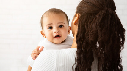 African Mom Posing With Adorable Baby Boy Carrying Cute Little Son In Arms Standing Back To Camera...