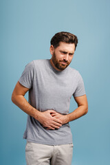 Portrait of sad Latin man having stomachache, diarrhea standing isolated on blue background