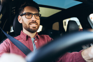 Smiling, handsome businessman wearing eyeglasses driving car, looking away. Transportation concept