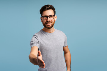 Smiling beautiful Latin man wearing stylish eyeglasses handshake, posing isolated on blue background