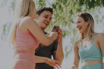 Three friends share a joyful moment outdoors, engaging in a lively chat during a sunny park workout. Their laughter and camaraderie highlight the essence of friendship and active living.