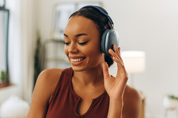 Fototapeta premium Portrait of a smiling woman listening to music with headphones while looking down in room