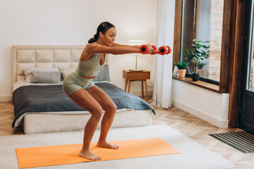 Fit young African American woman using dumbbells training at home in bedroom