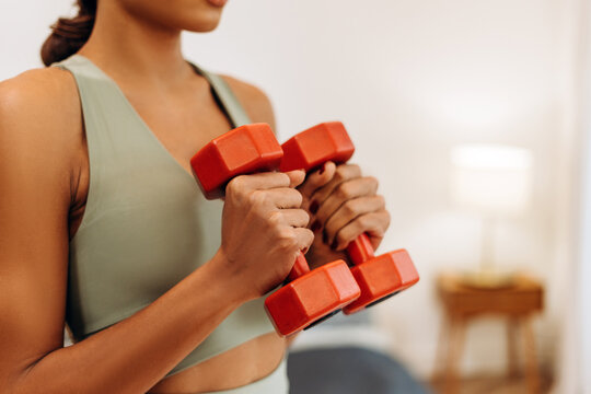 Young African American woman exercising at home in a living room, holding dumbbells