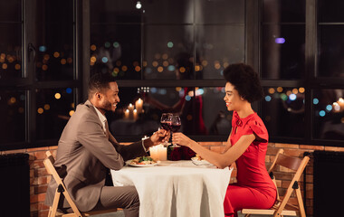 Happy Black Couple Clinking Glasses Drinking Wine And Celebrating Valentine's Day In Restaurant In Evening. Side View