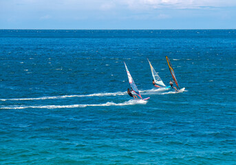 Three men on windsurfers catch the wind on the sea in clear, windy weather. Sporting activity,...