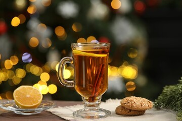 Hot tea with lemon, cinnamon and tasty cookies on table against blurred Christmas lights, bokeh effect