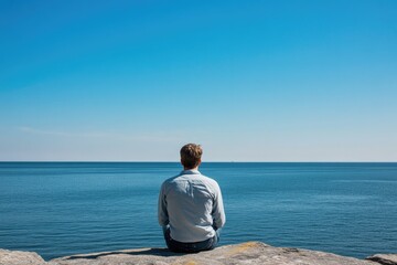 A person sitting on a rocky outcropping, gazing out at the vast ocean - Powered by Adobe