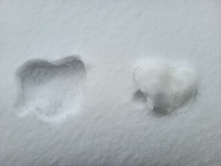 There is a heart made of snow on the white snow and a hole in the shape of a heart next to it.