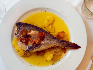 Steam-cooked fish with potatoes, tomatoes and pepper dressed with sauce dished up in a plate