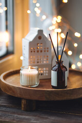 Christmas home aromatherapy. Aroma diffuser with organic essential oil, cinnamon, anise, vanilla scent, burning candles on wooden tray. Cozy atmosphere, holiday spirit. Winter inspiration and mood